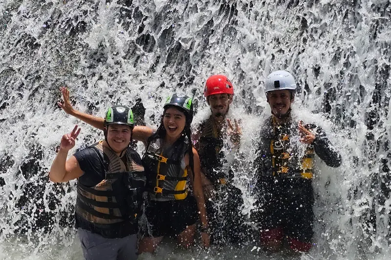 Four guests in helmets and life jackets in whitewater beneath a waterfall, south side of El Yunque