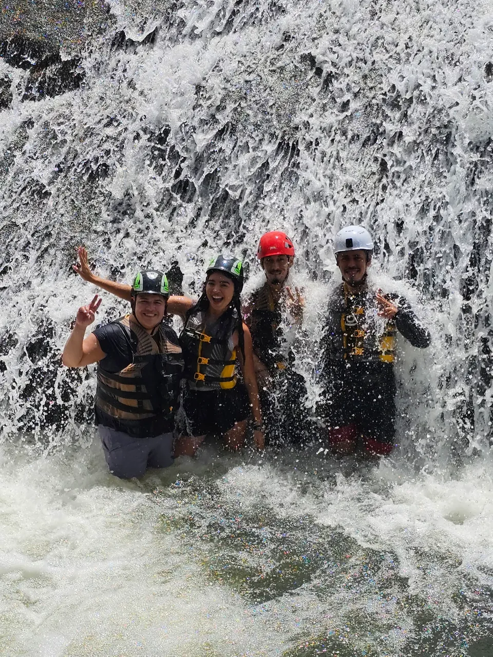 Four guests in helmets and life jackets standing in whitewater beneath a waterfall, El Yunque
