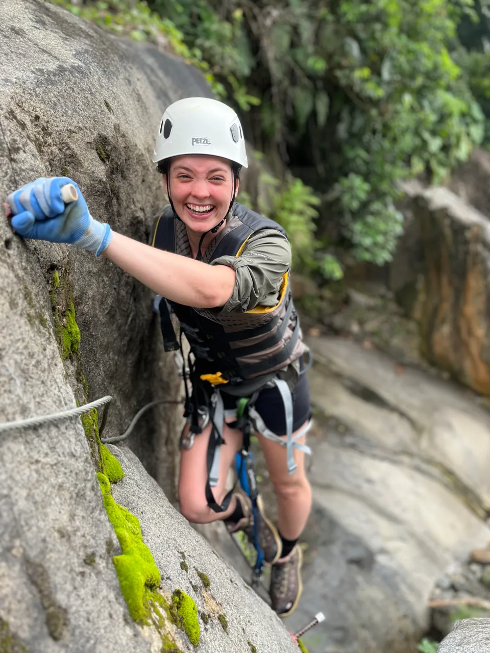 Climber in a harness and helmet on steel cable and rungs fixed to a rock face in El Yunque