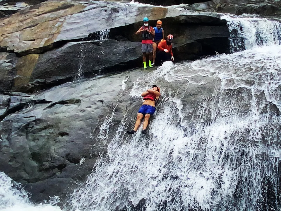 Two guests riding a natural rock slide into a river pool on the south side of El Yunque